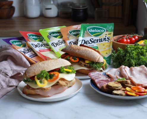 Alt text: Sandwich cu dovlecei pane, mortadella, cașcaval DeSenviș, pesto și legume proaspete, servit în chiflă crocantă.