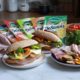 Alt text: Sandwich cu dovlecei pane, mortadella, cașcaval DeSenviș, pesto și legume proaspete, servit în chiflă crocantă.