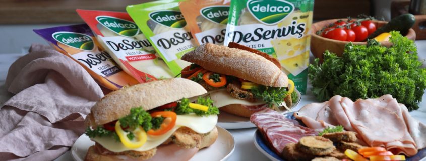 Alt text: Sandwich cu dovlecei pane, mortadella, cașcaval DeSenviș, pesto și legume proaspete, servit în chiflă crocantă.
