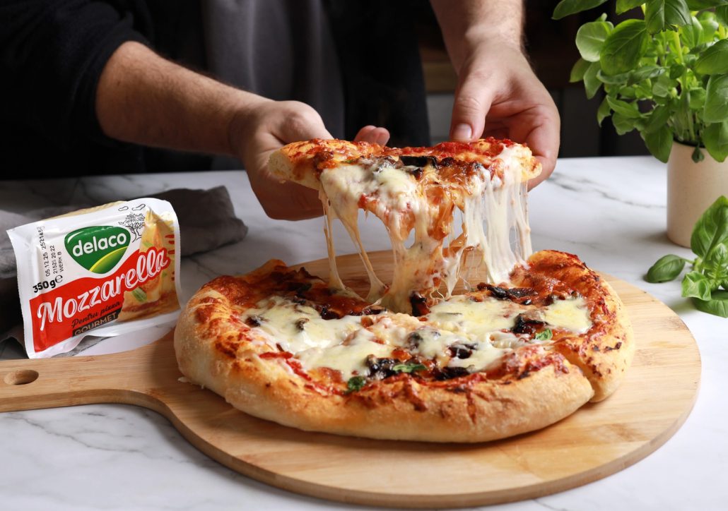 Felie de pizza cu ceapă caramelizată, bacon și mozzarella Delaco care se întinde